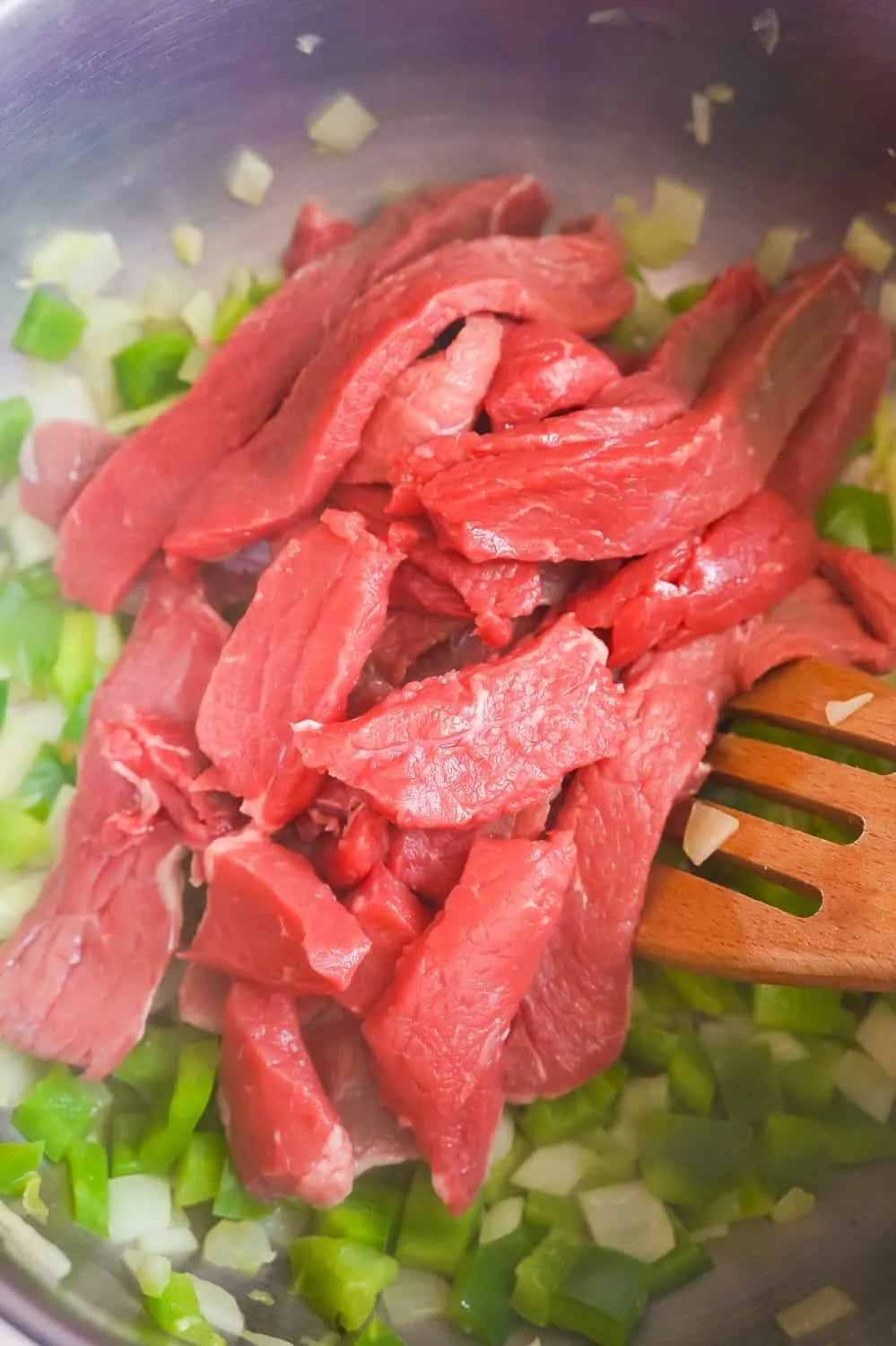 raw steak strips added to a frying pan with diced green peppers