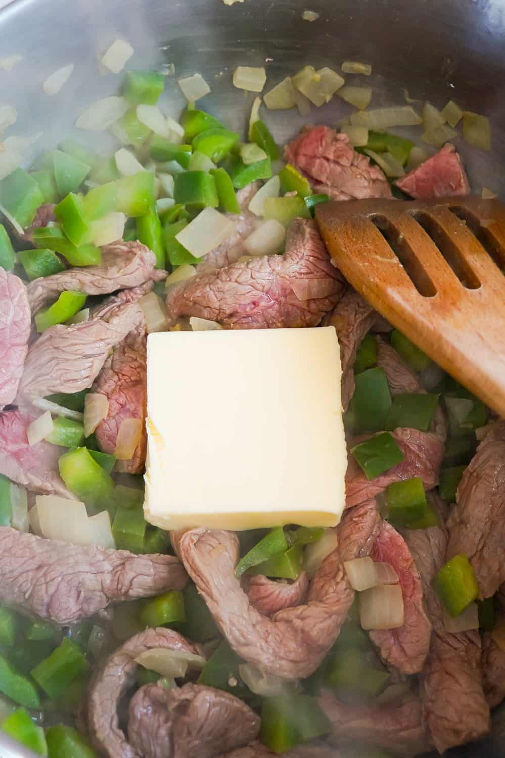 butter added to a frying pan with steak strips and diced green peppers