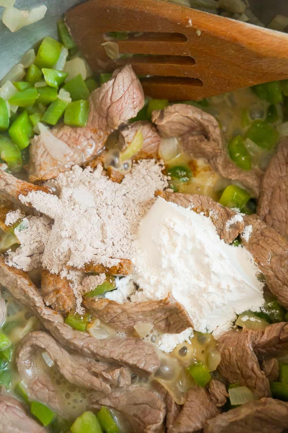 flour and powdered beef gravy mix added to a frying pan with steak strips and diced green peppers