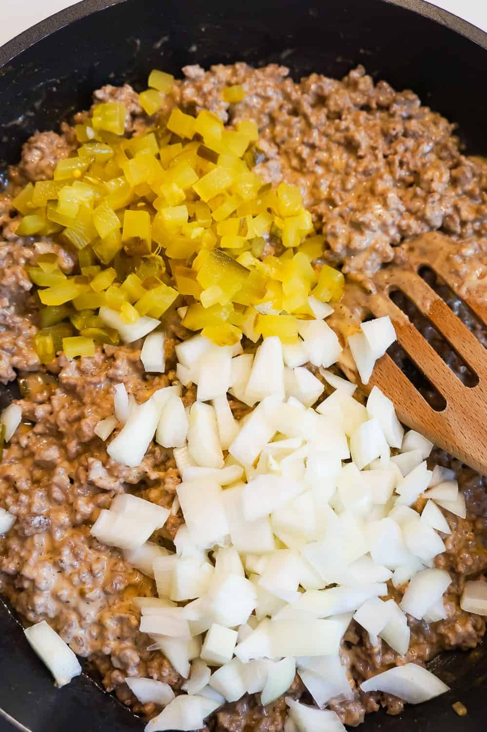 diced pickles and diced onions on top of ground beef mixture on a frying pan