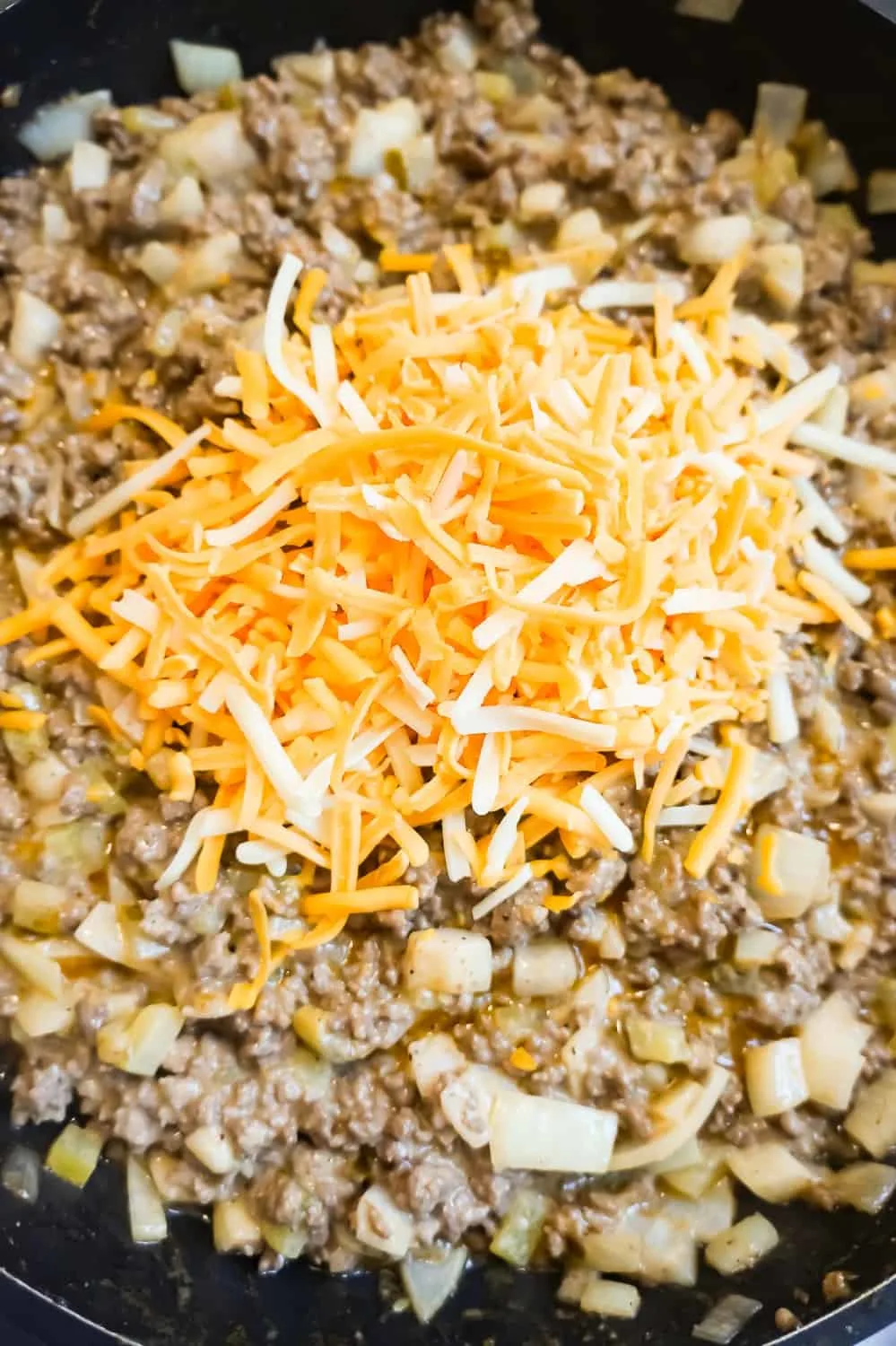 shredded cheddar cheese on top of ground beef mixture in a frying pan