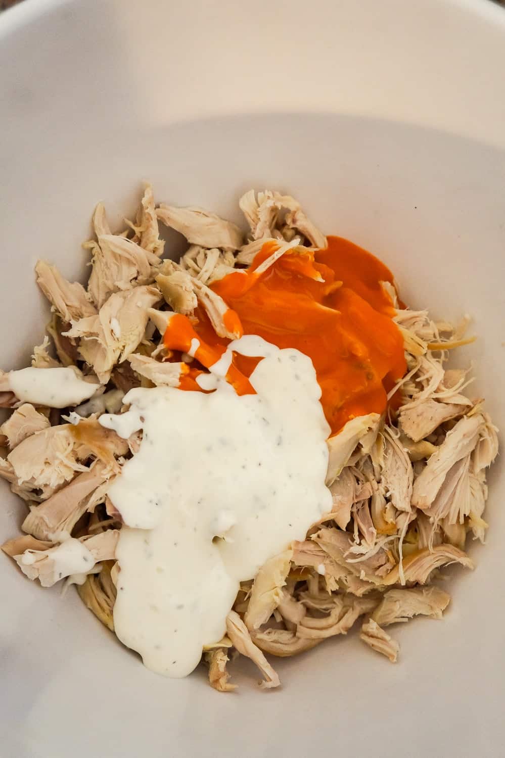 shredded chicken in a mixing bowl with Buffalo sauce and ranch dressing