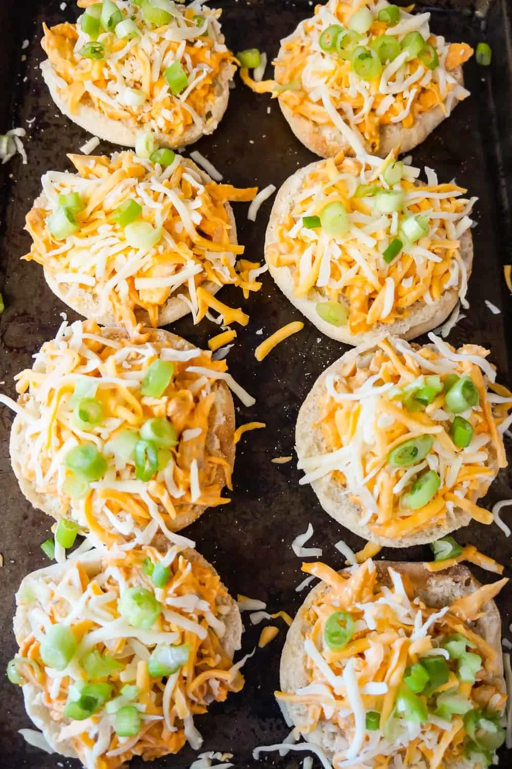 Buffalo chicken English Muffins topped with shredded cheese before baking