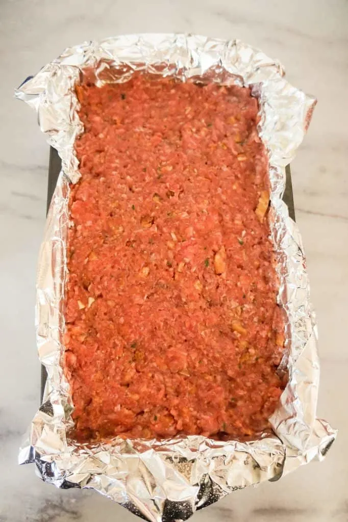raw meatloaf mixture pressed into a foil lined loaf pan