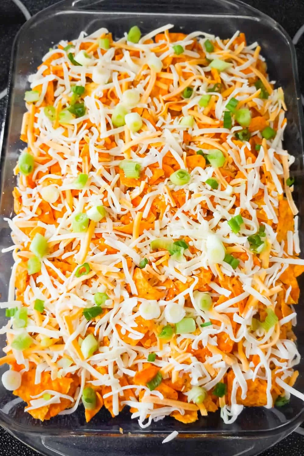 shredded cheese and chopped green onions on top of crumbled Doritos