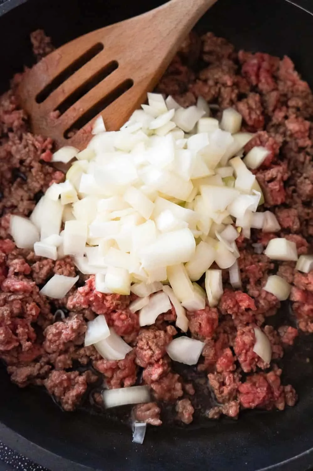 diced onion on top of raw ground beef in a frying pan