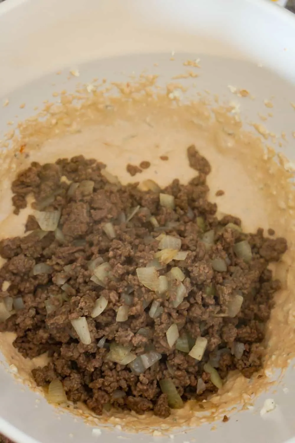 cooked ground beef and onion on top of cream cheese mixture in a mixing bowl.