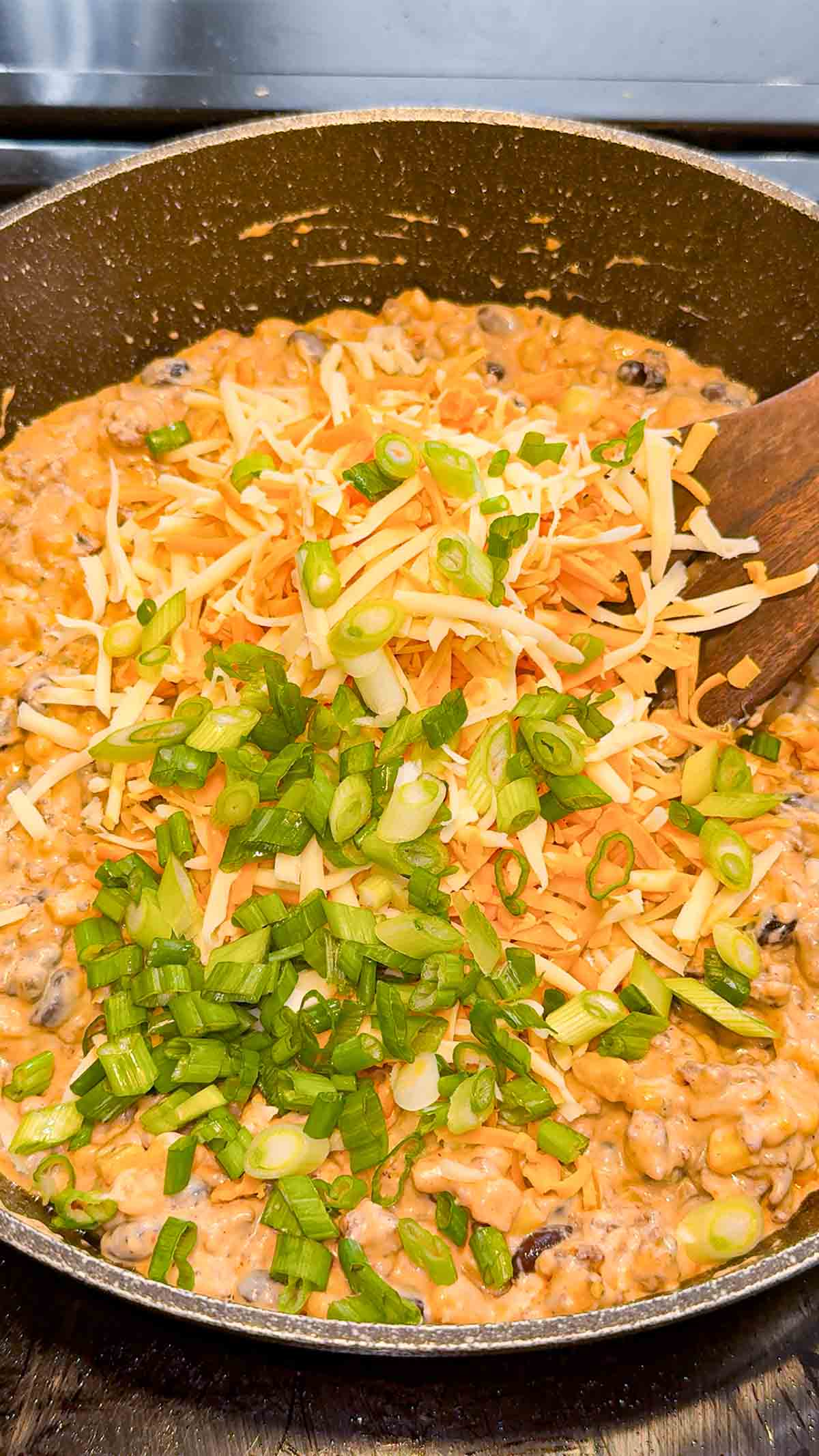 chopped green onions and shredded cheese on top of creamy ground beef mixture in a skillet