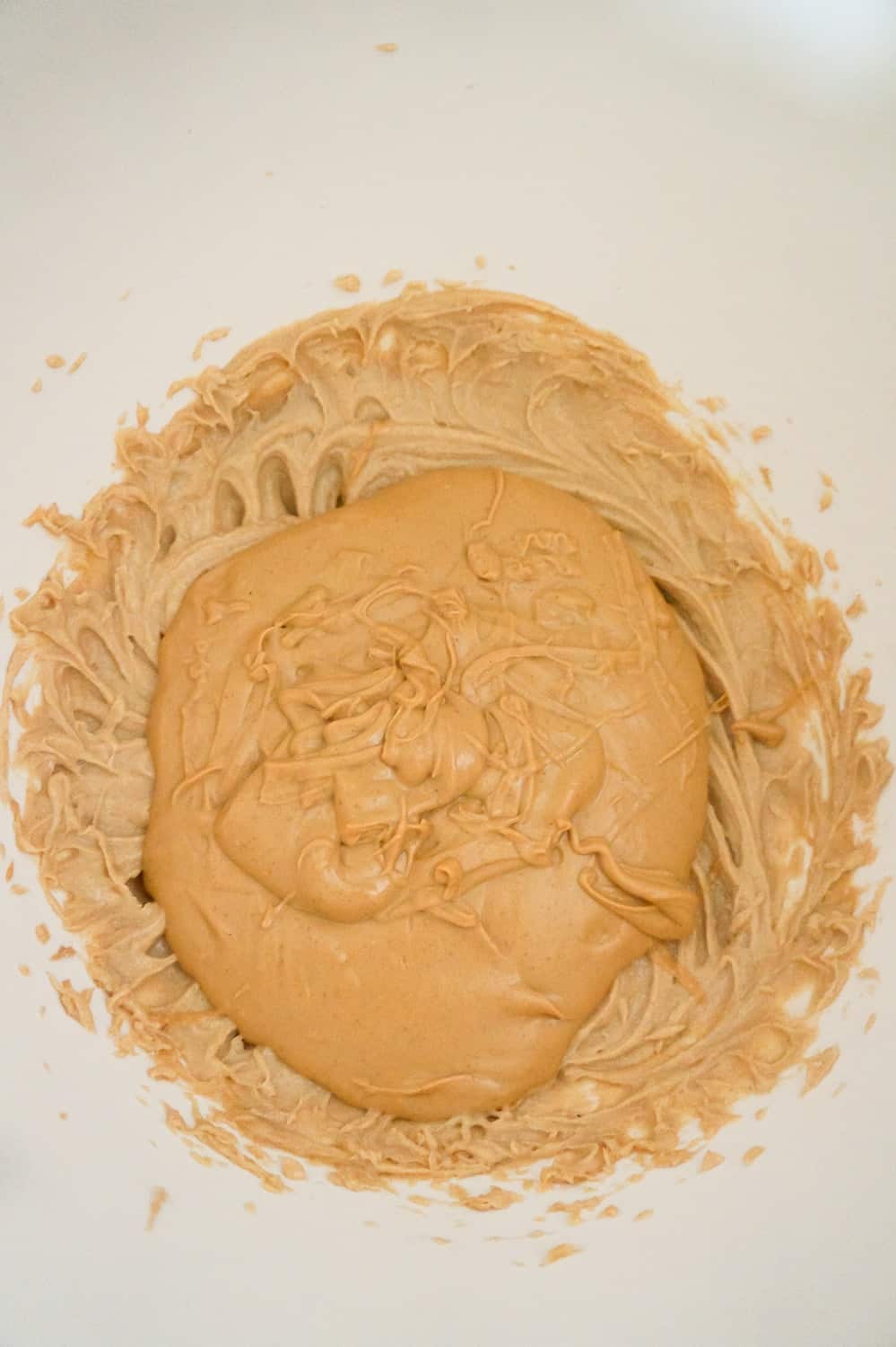 melted peanut butter baking chips on top of peanut butter mixture in a mixing bowl