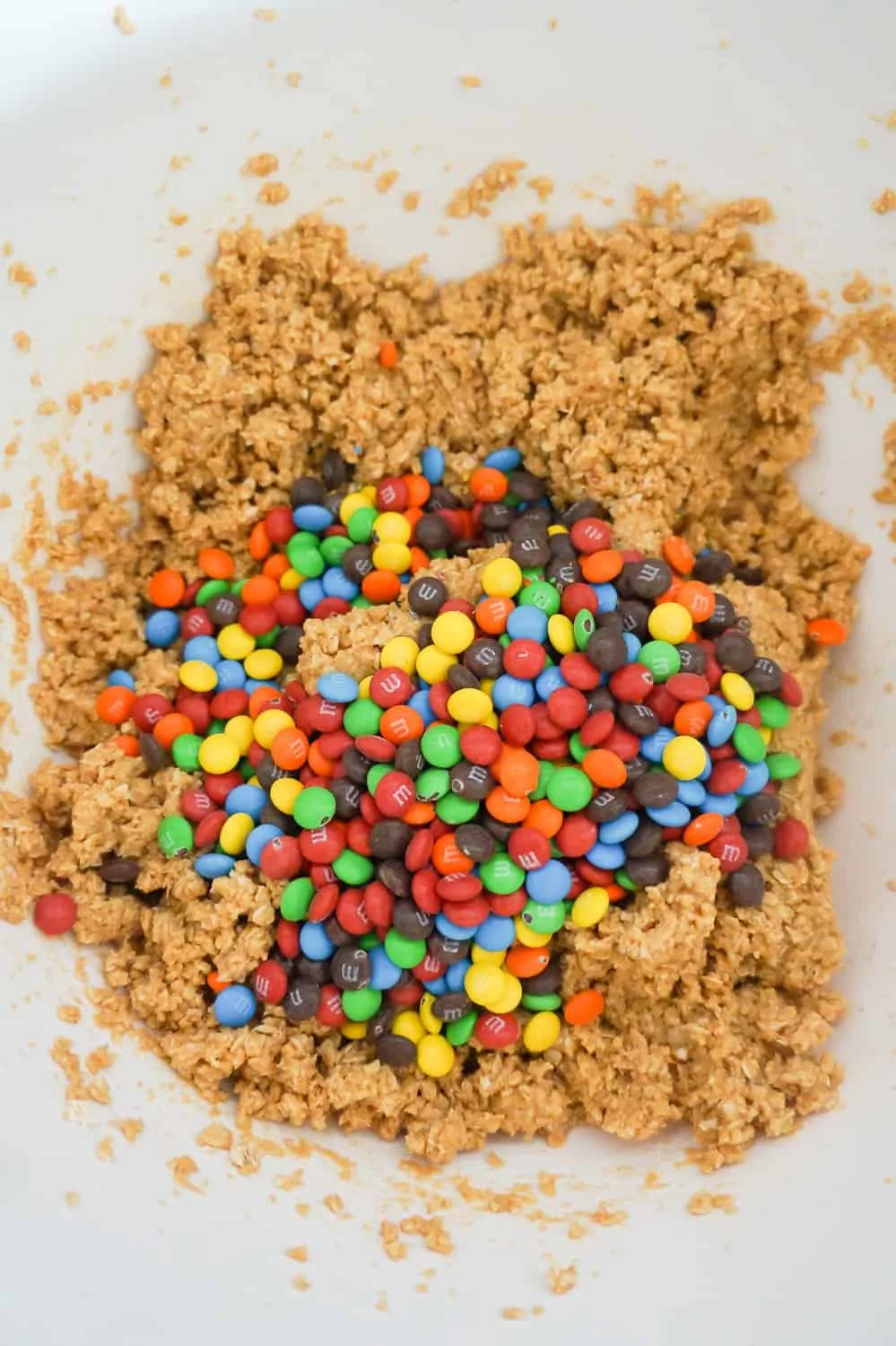 mini M&M's on top of peanut butter oatmeal cookie dough in a mixing bowl
