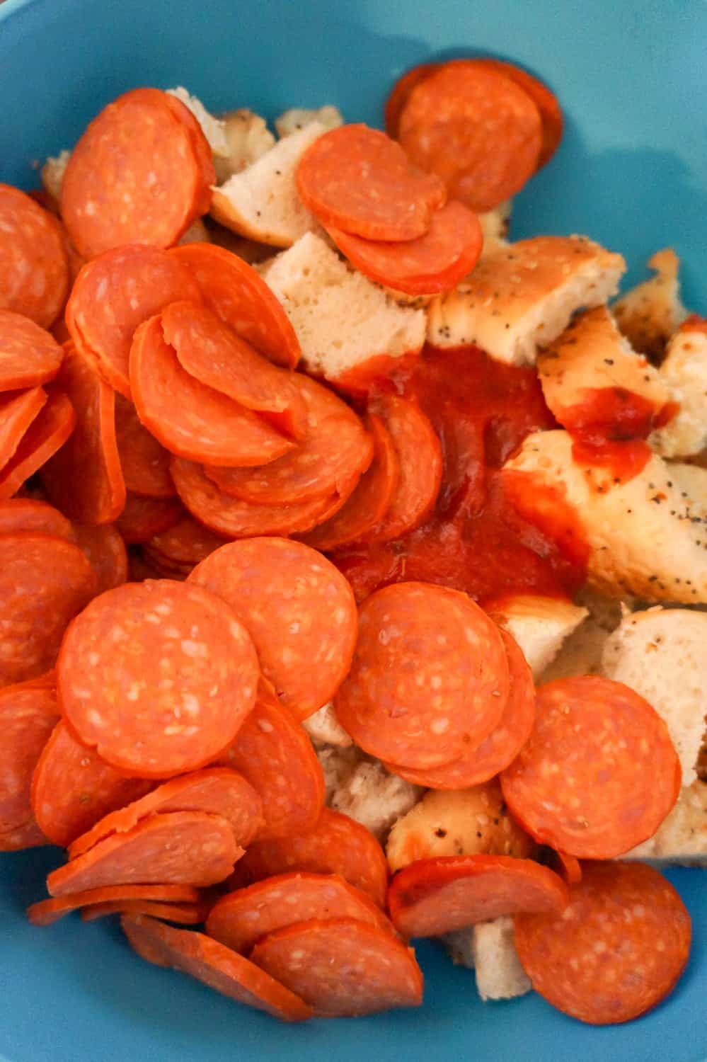 pepperoni slices, pizza sauce and bagel pieces in a large mixing bowl