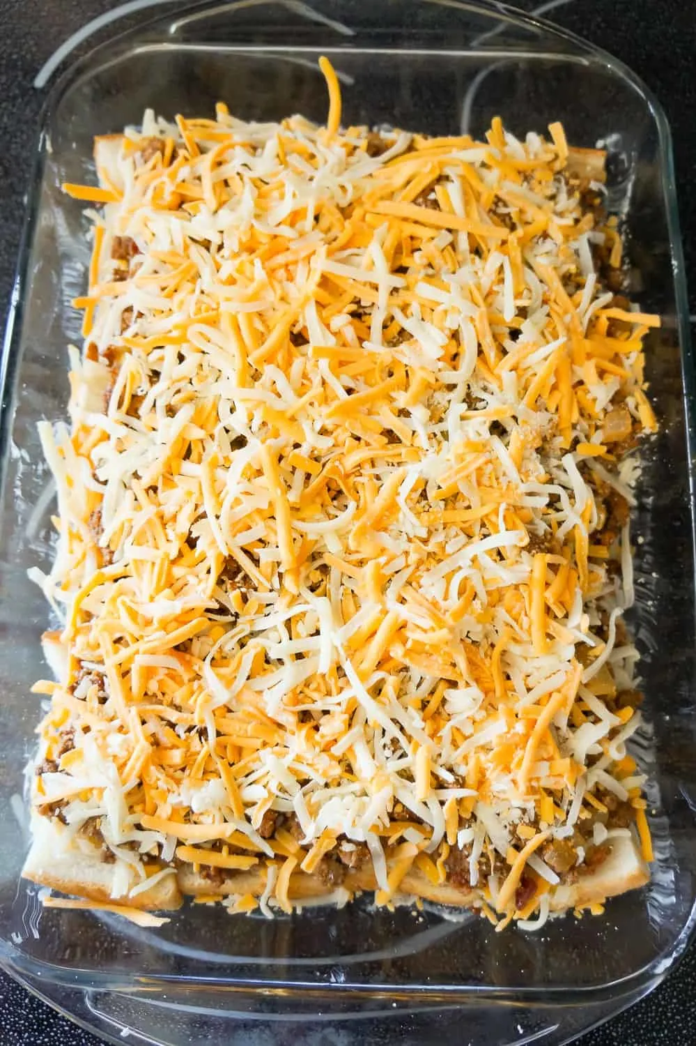 shredded mozzarella and cheddar on top of ground beef mixture in a baking dish