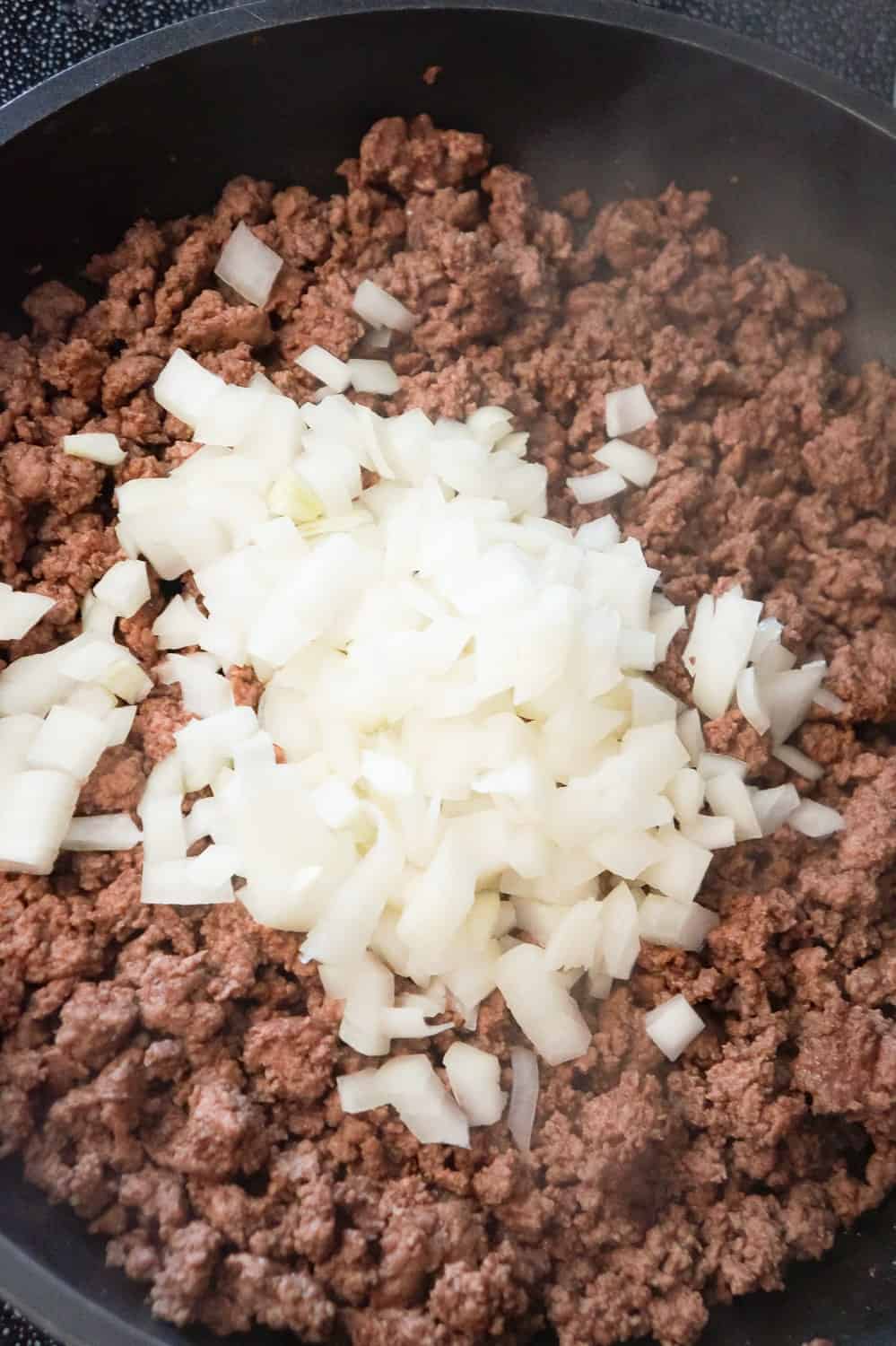 diced onions on top of ground beef in a frying pan