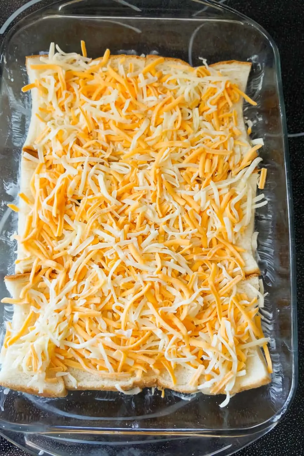 shredded mozzarella and cheddar on top of bread in a baking dish