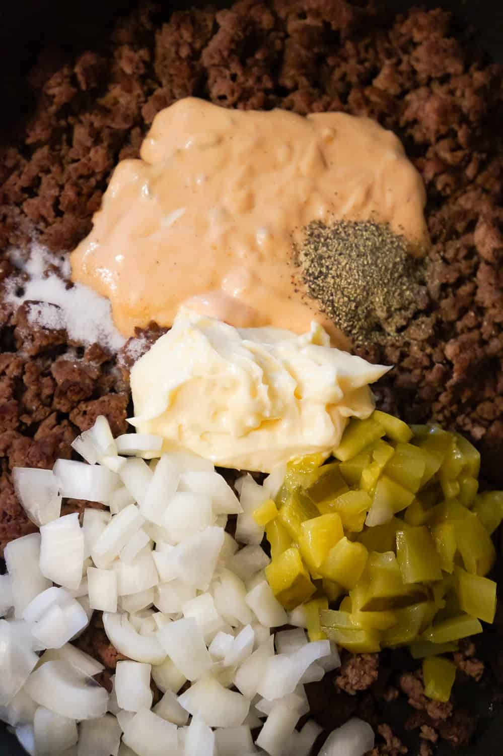 diced onions, diced pickles, mayo, Thousand Island dressing, salt and pepper on top of cooked ground beef in a frying pan