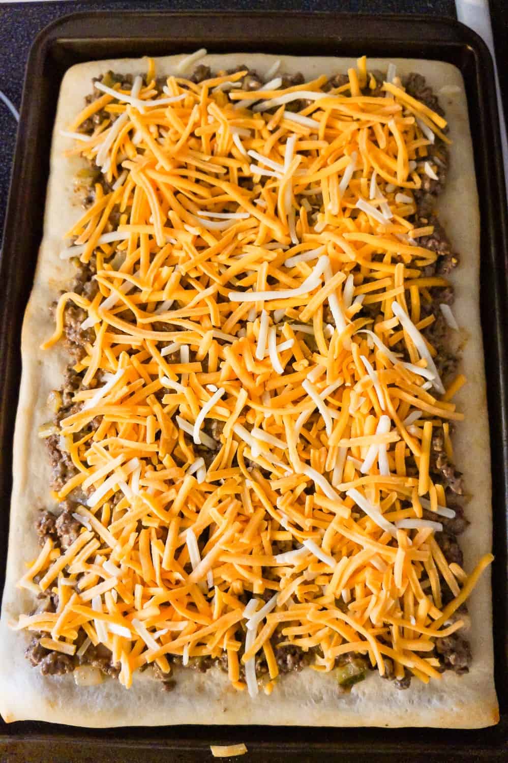 shredded cheddar cheese on top of big mac pizza before baking