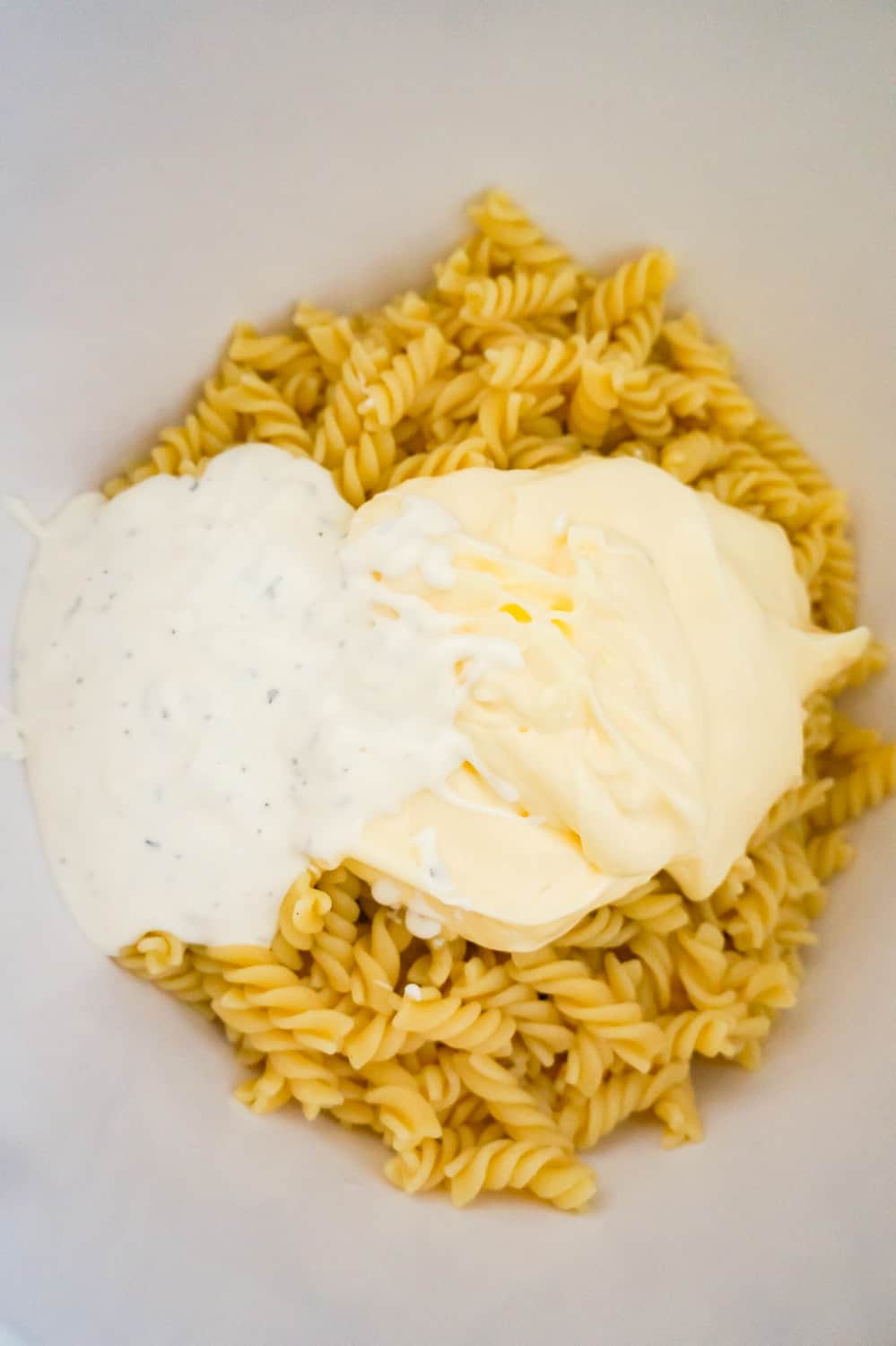 mayo and ranch dressing on top of cooked pasta in a mixing bowl