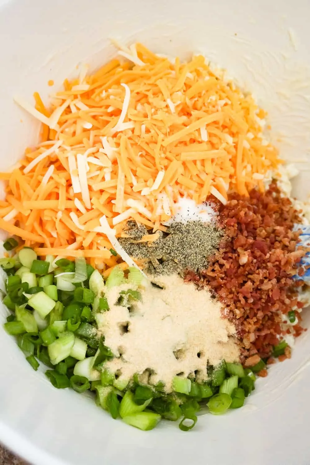 shredded cheddar cheese, chopped green onions, bacon bits and spices in a mixing bowl