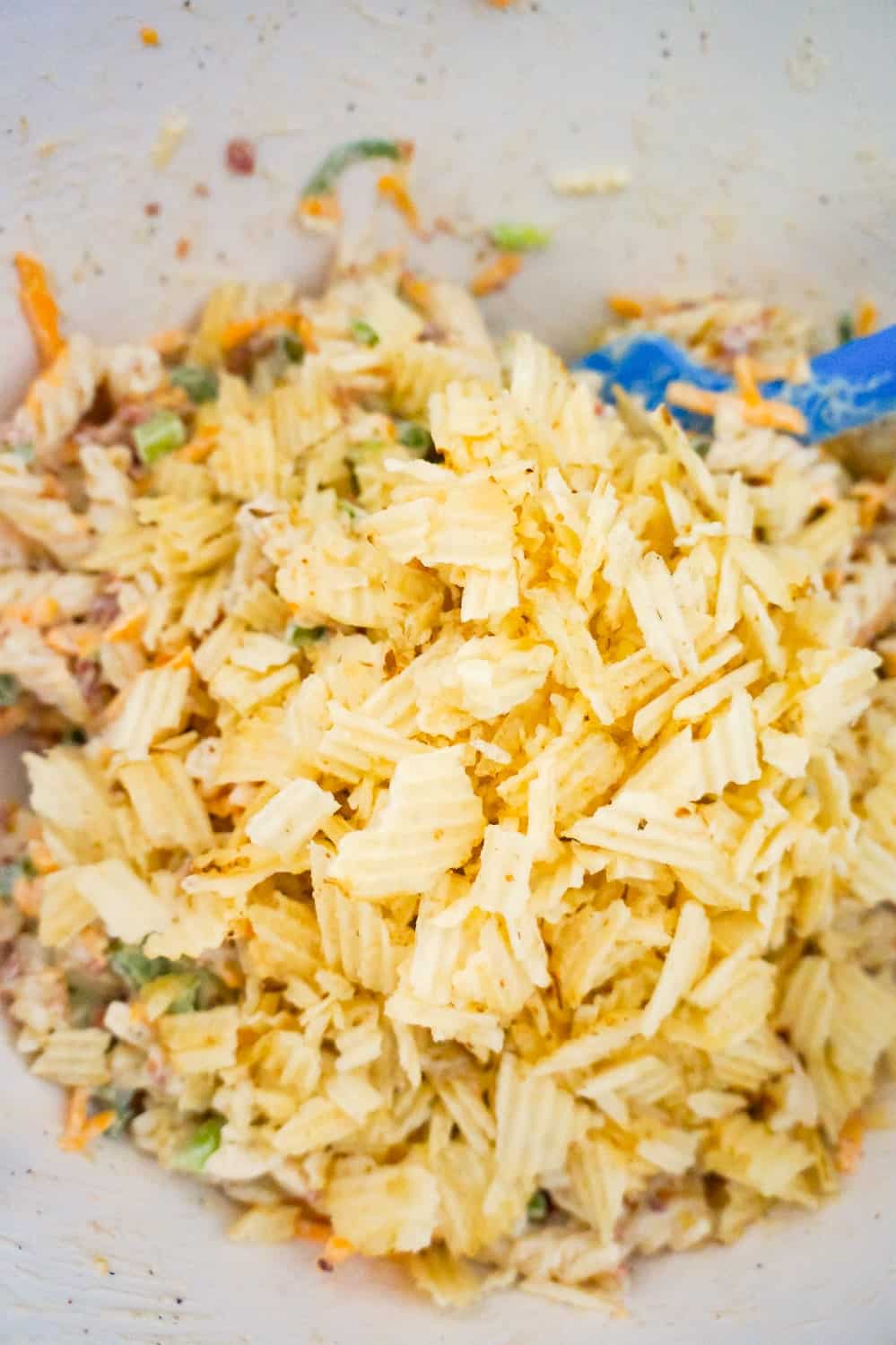 crumbled potato chips on top of pasta salad in a mixing bowl