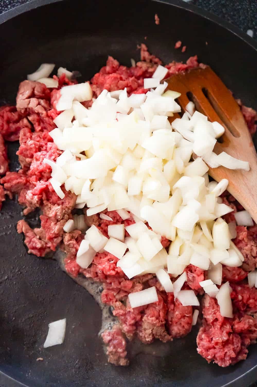 diced onions on top of raw ground beef in a frying pan