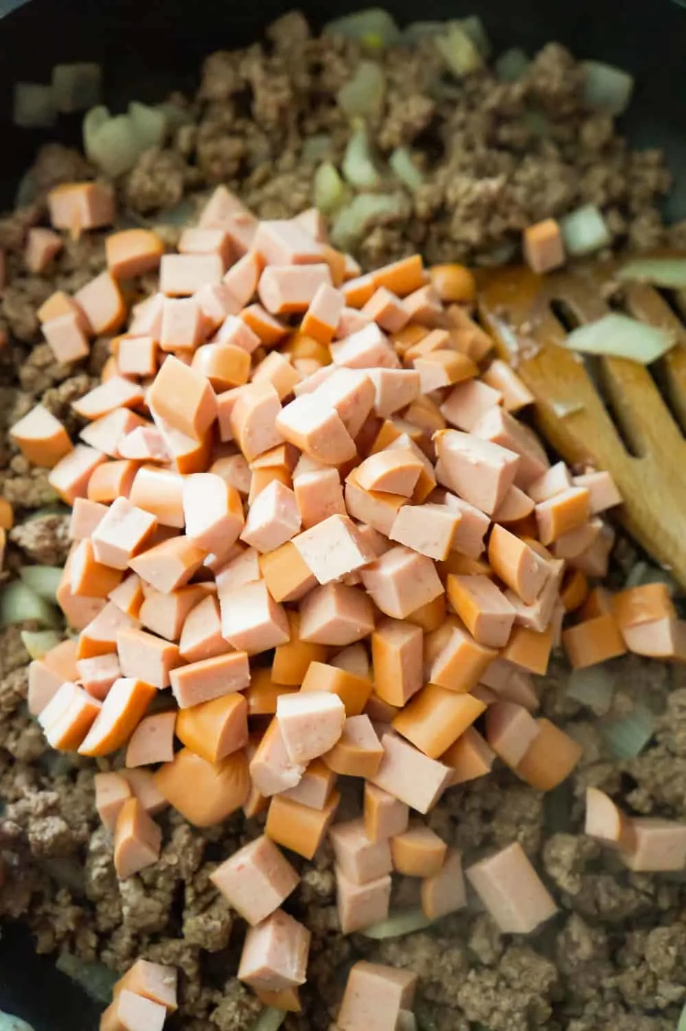 diced wieners on top of ground beef mixture in a frying pan