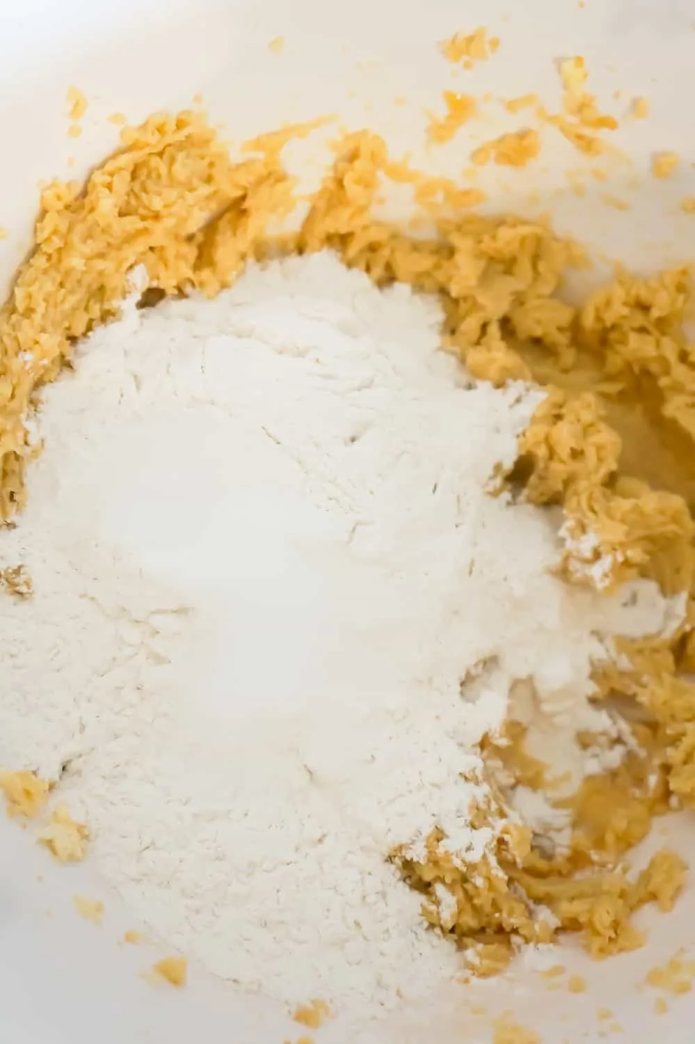 flour on top of butter and sugar mixture in a mixing bowl