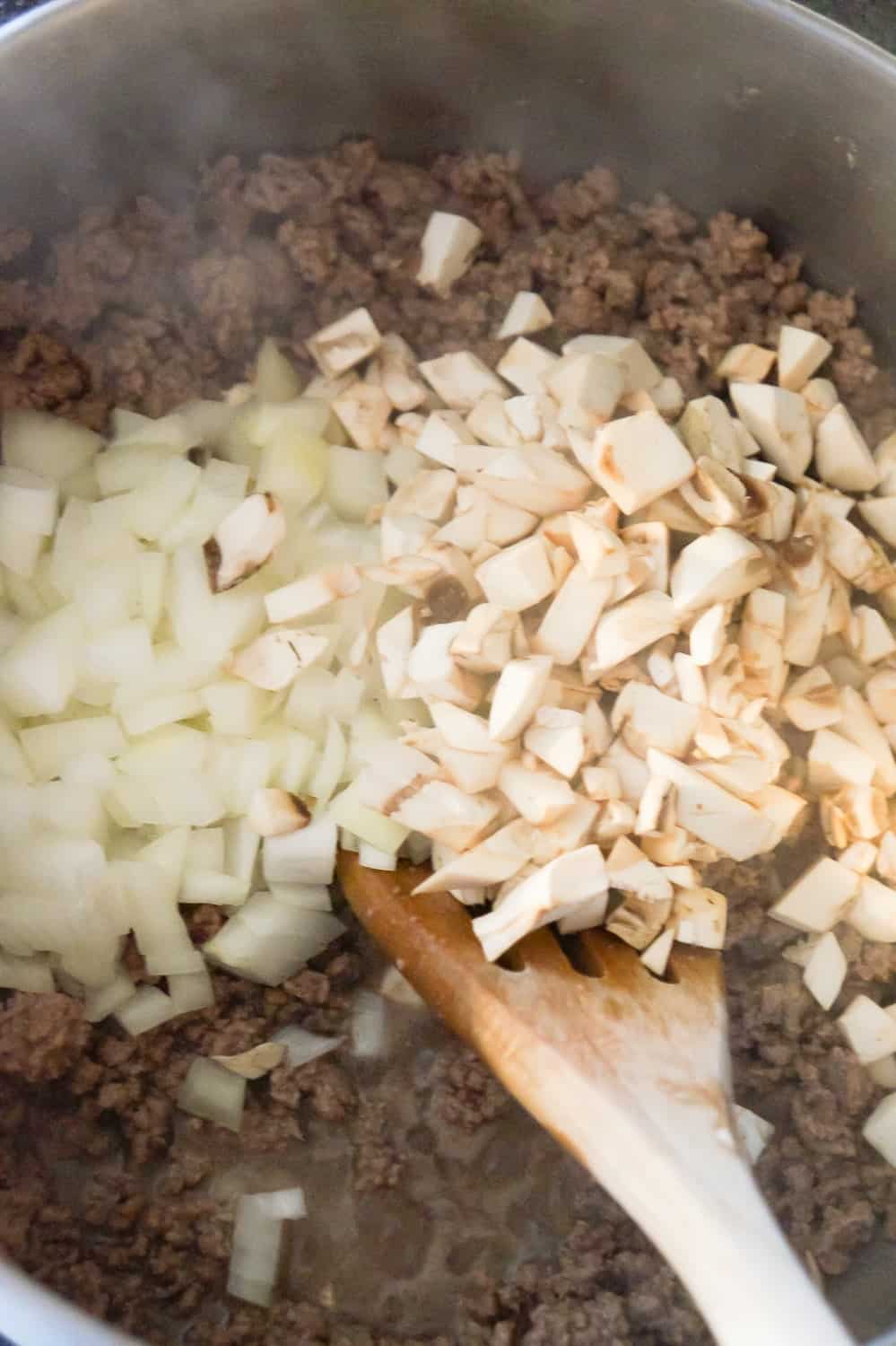 diced onions and diced mushrooms on top of cooked ground beef in a pot