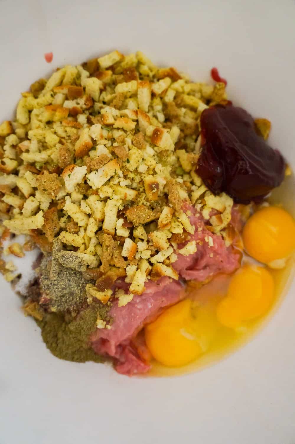 stove top stuffing mix, cranberry sauce and eggs on top of ground turkey in a mixing bowl