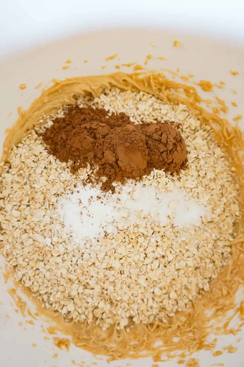 cocoa powder, baking powder and quick oats on top of creamy peanut butter mixture in a mixing bowl