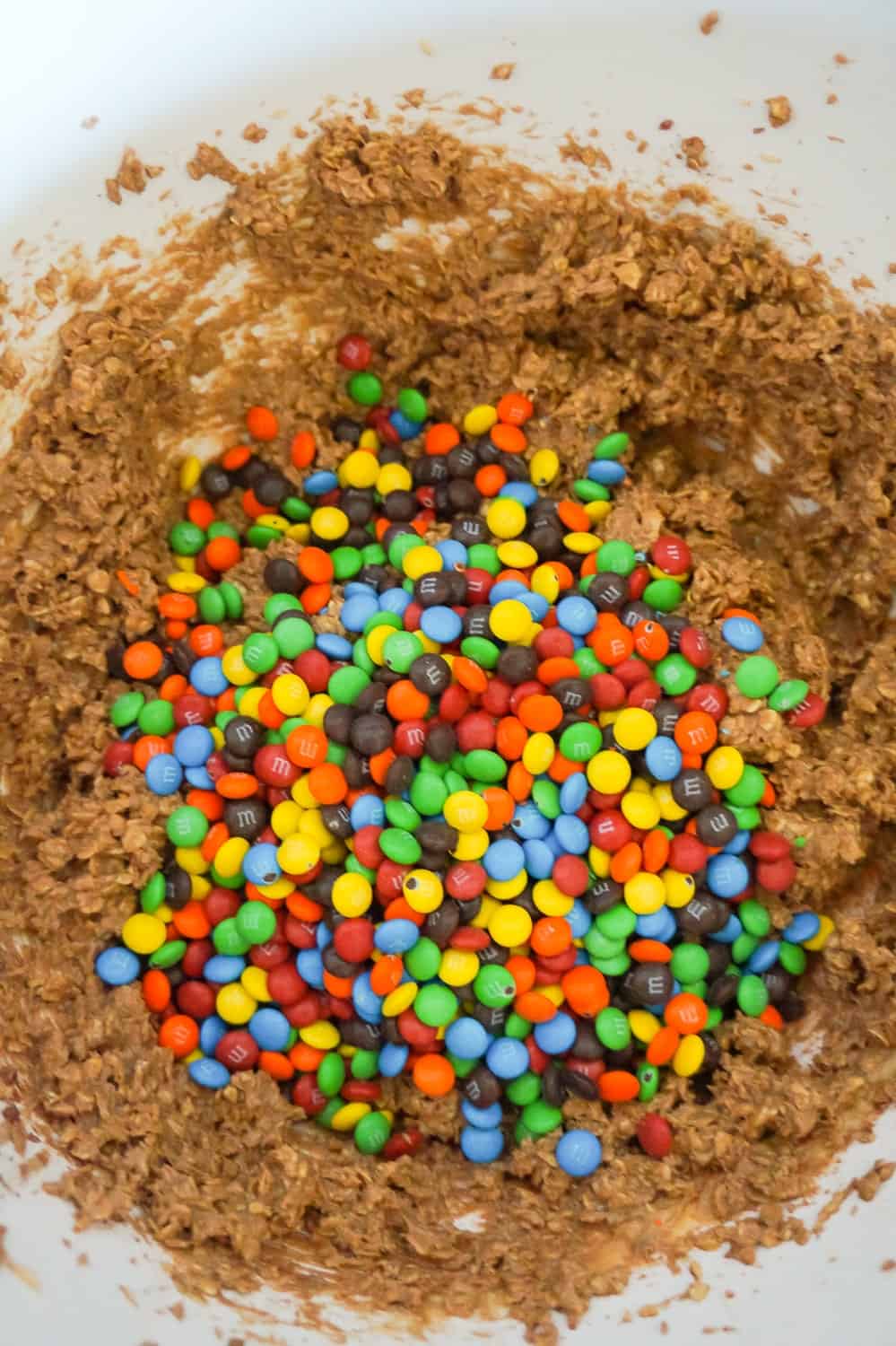 mini M&M's on top of chocolate peanut butter oatmeal cookie dough in a mixing bowl