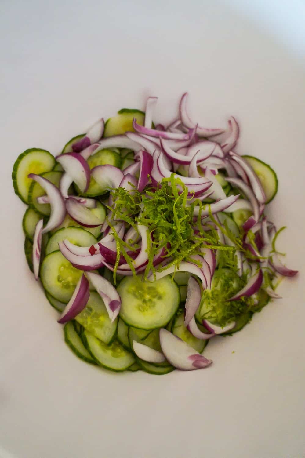 thinly sliced cucumbers, red onions and lime zest in a bowl