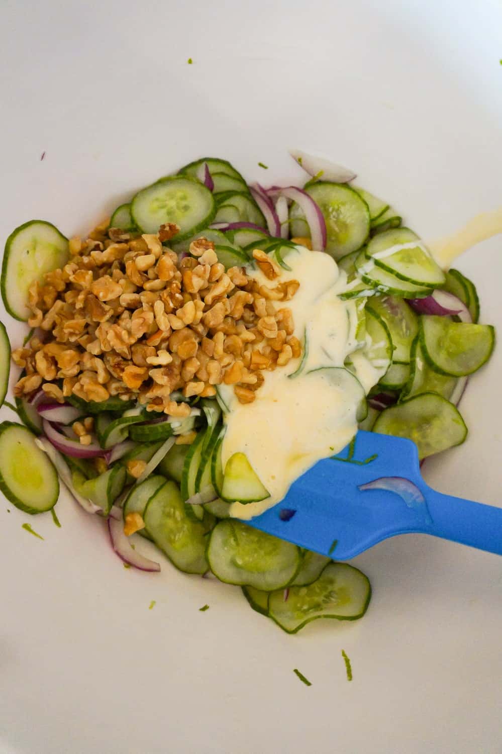 thinly sliced cucumbers, red onions, chopped walnuts and coleslaw dressing in a bowl