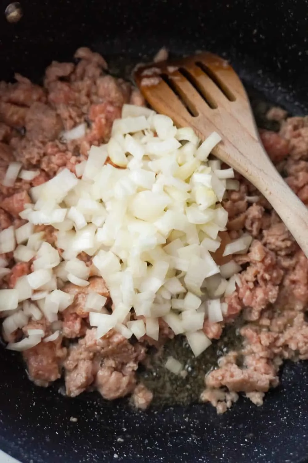 diced onions on top of raw ground sausage meat in a frying pan