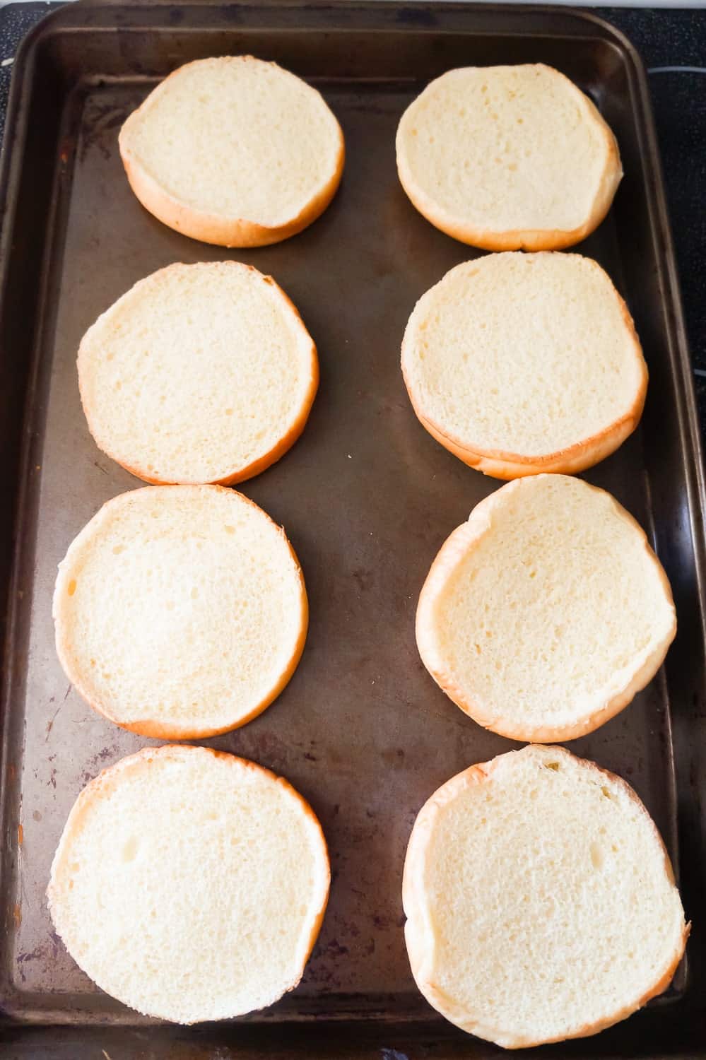 hamburger buns laying in a single layer on a baking sheet