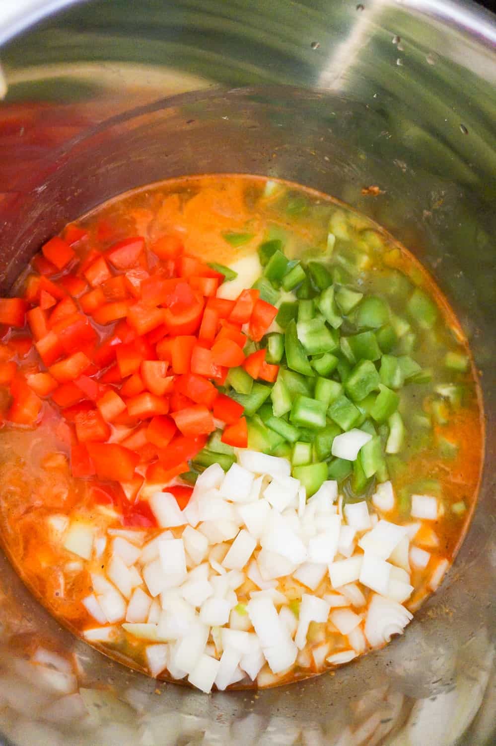 diced red peppers, diced green peppers and diced onions on top of chicken and broth in an Instant Pot
