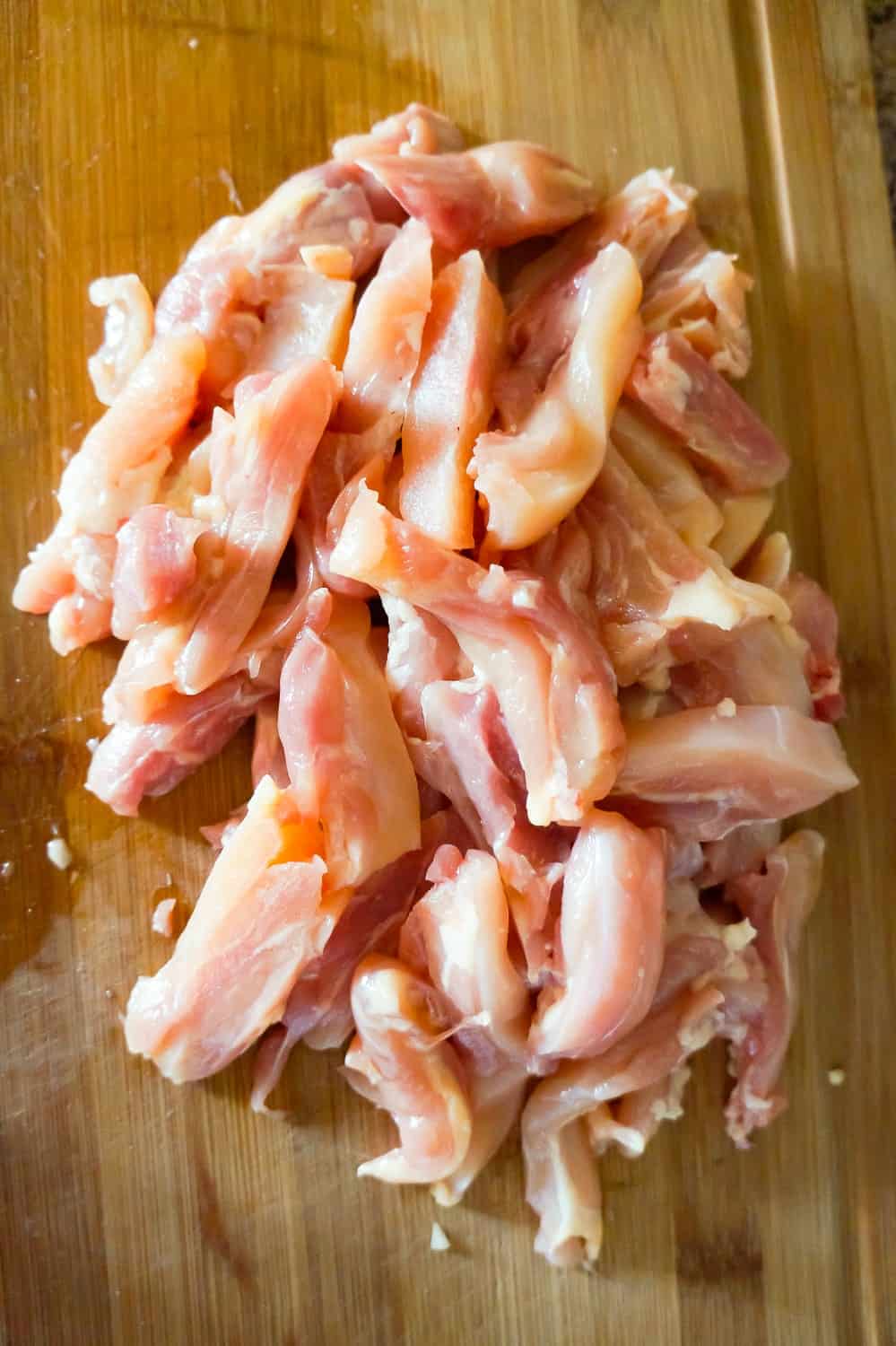 raw chicken thigh strips on a cutting board