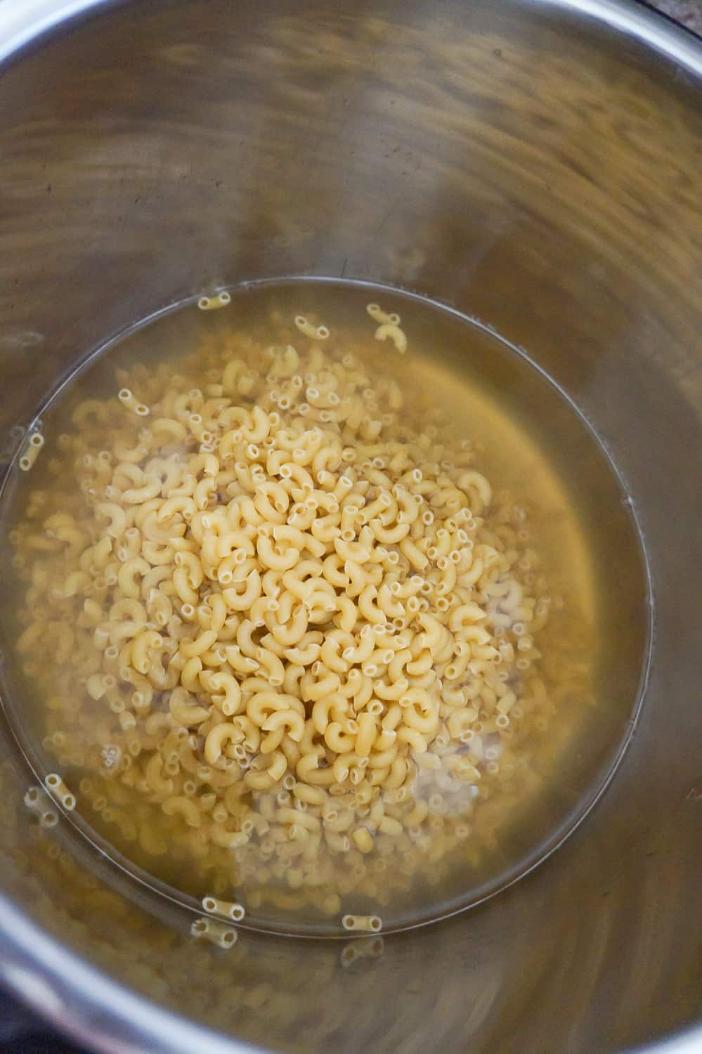 uncooked macaroni noodles in liquid in an Instant Pot