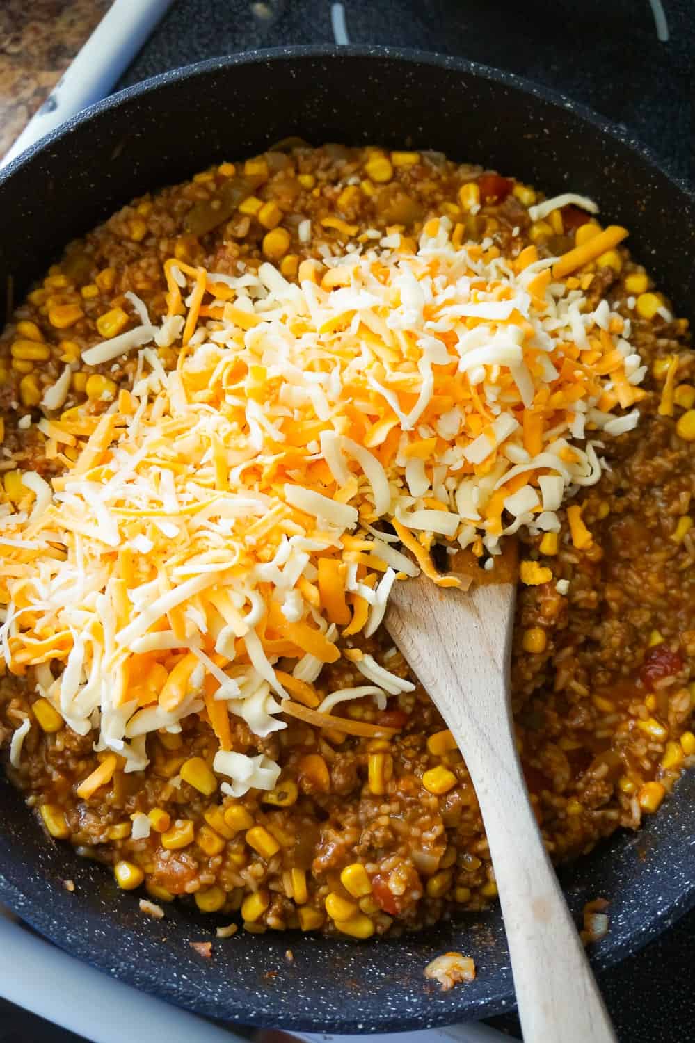 shredded mozzarella and cheddar cheese on top of ground beef in a skillet