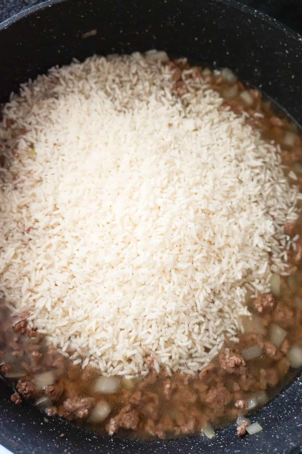 uncooked minute rice on top of ground beef in a skillet