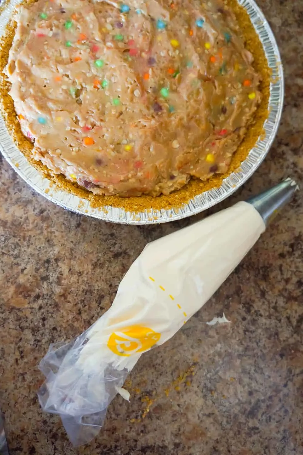 piping bag with cream cheese frosting beside no bake monster cookie dough cheesecake