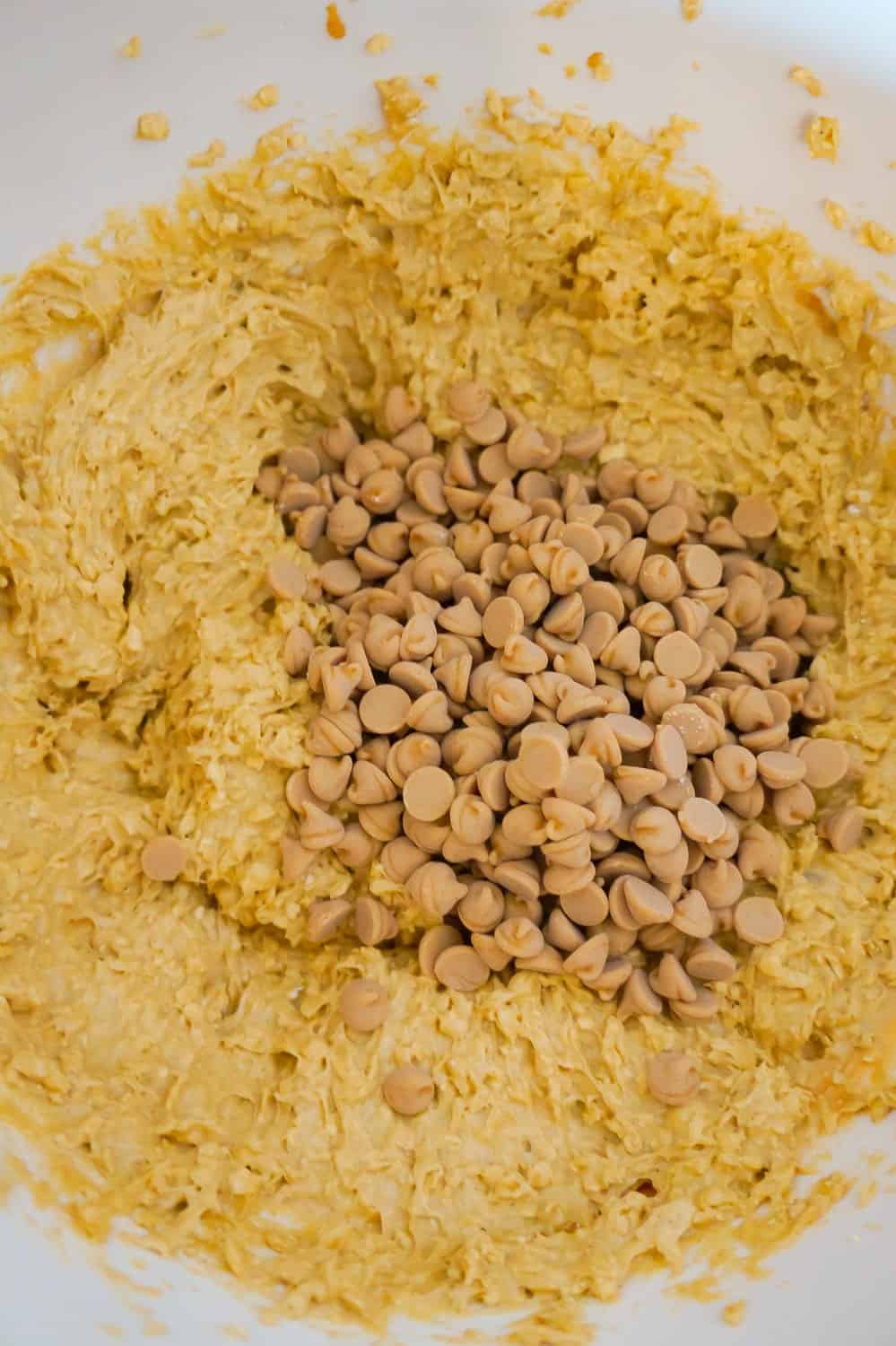peanut butter baking chips on top of peanut butter oatmeal muffin batter in a mixing bowl