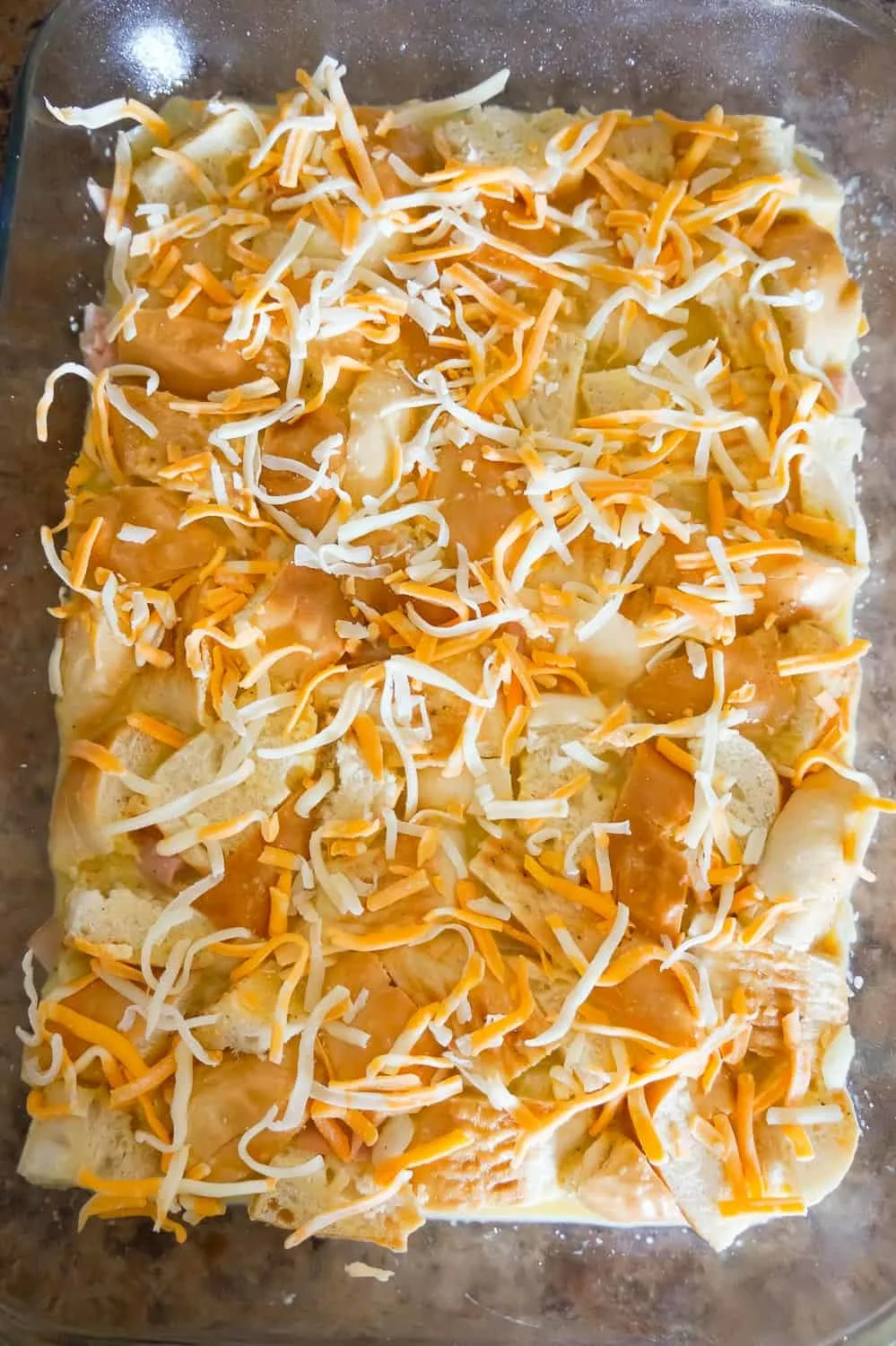 shredded cheese on top of chopped bagels in an egg mixture in a baking dish