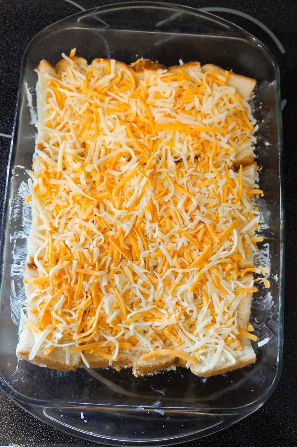 shredded mozzarella and cheddar cheese on top of bread in a baking dish