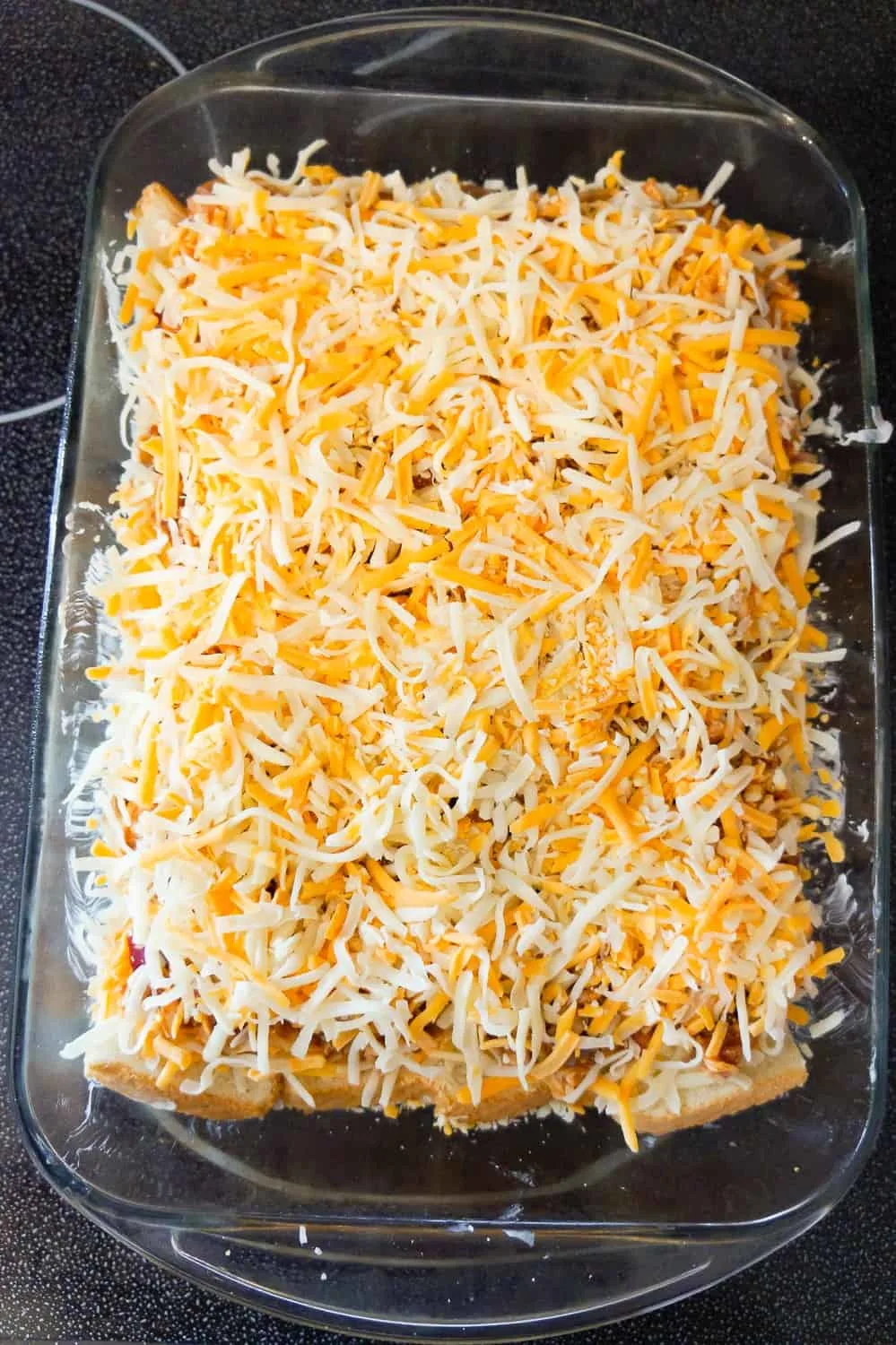 shredded mozzarella and cheddar cheese on top of chicken mixture in a baking dish