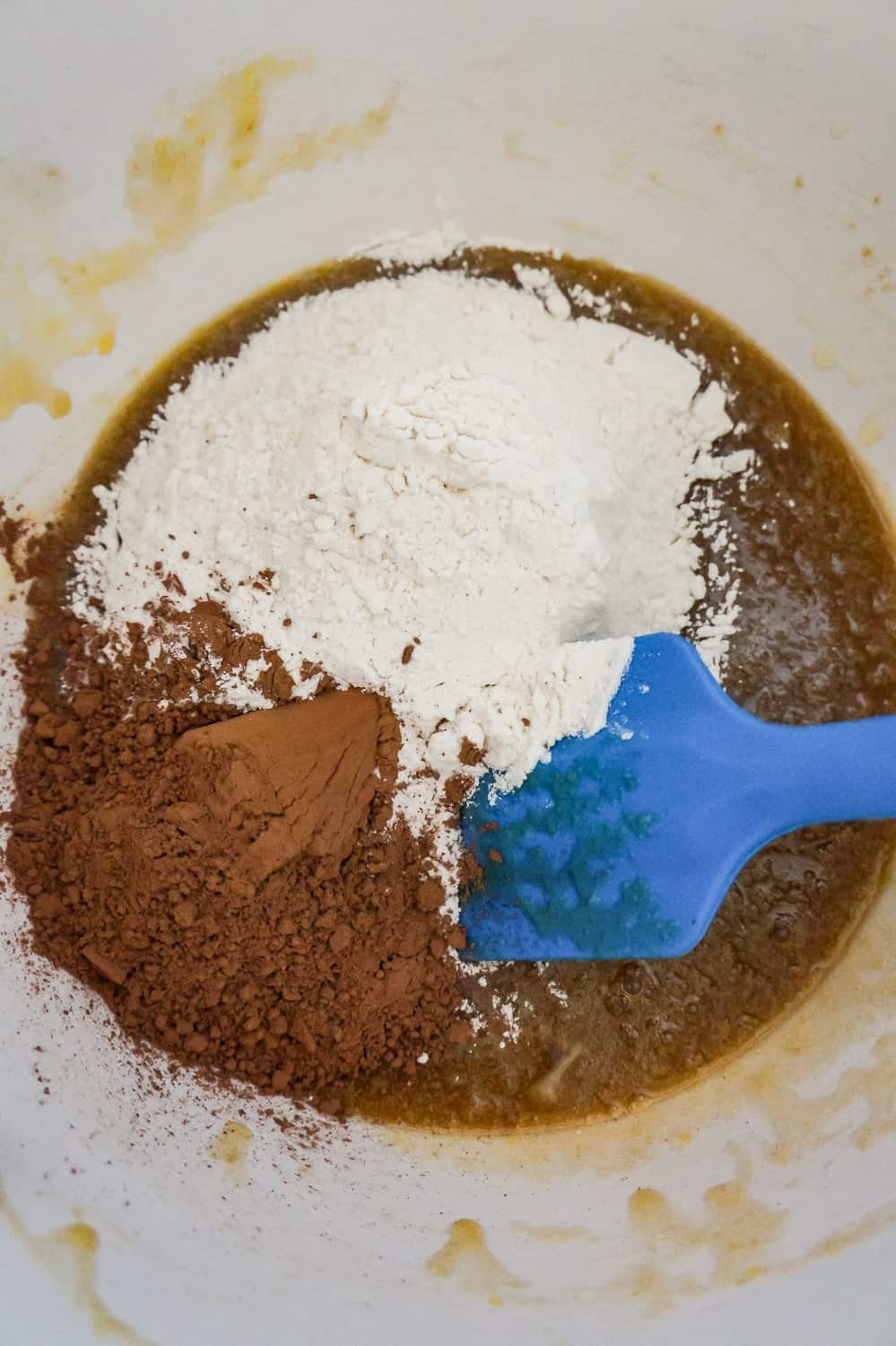 flour and cocoa powder on top of butter and egg mixture in a mixing bowl