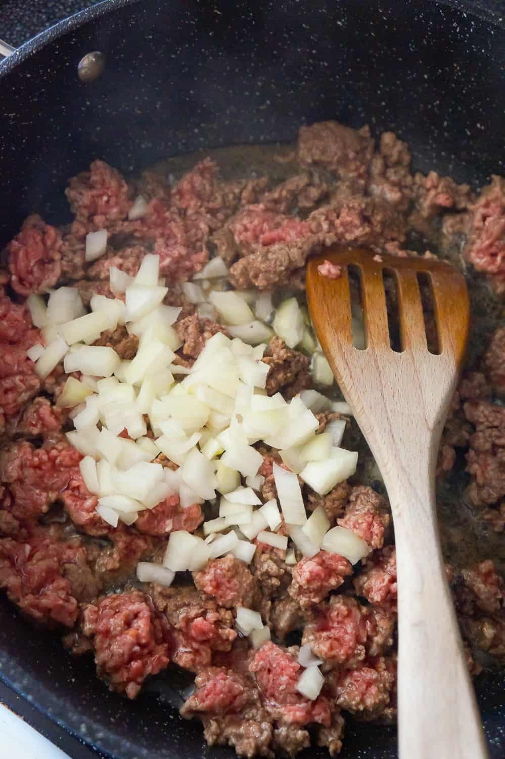 diced onion on top of ground beef in a saute pan