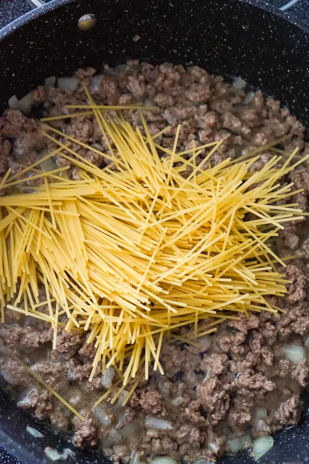 uncooked spaghetti noodles on top of ground beef and water in a saute pan