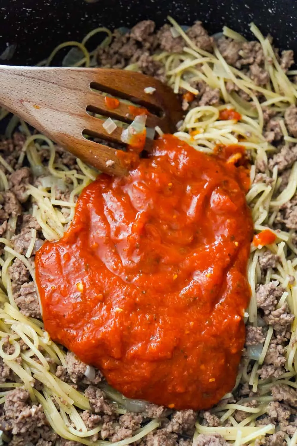 marinara sauce on top of spaghetti and ground beef in a pan
