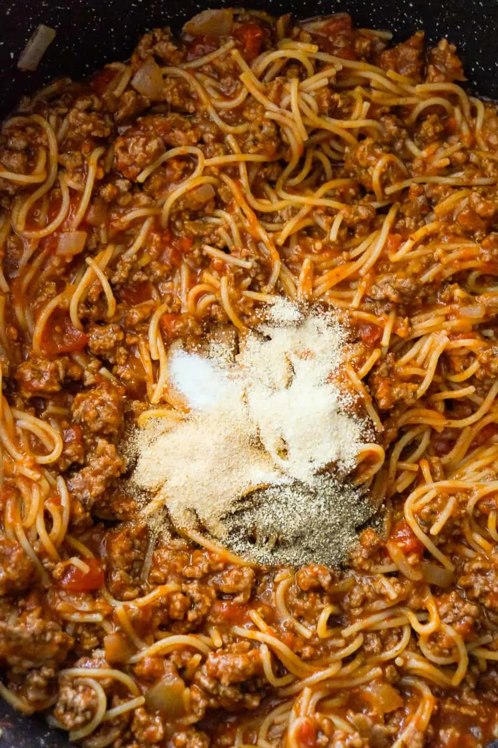 spices on top of spaghetti bolognese in a pan.