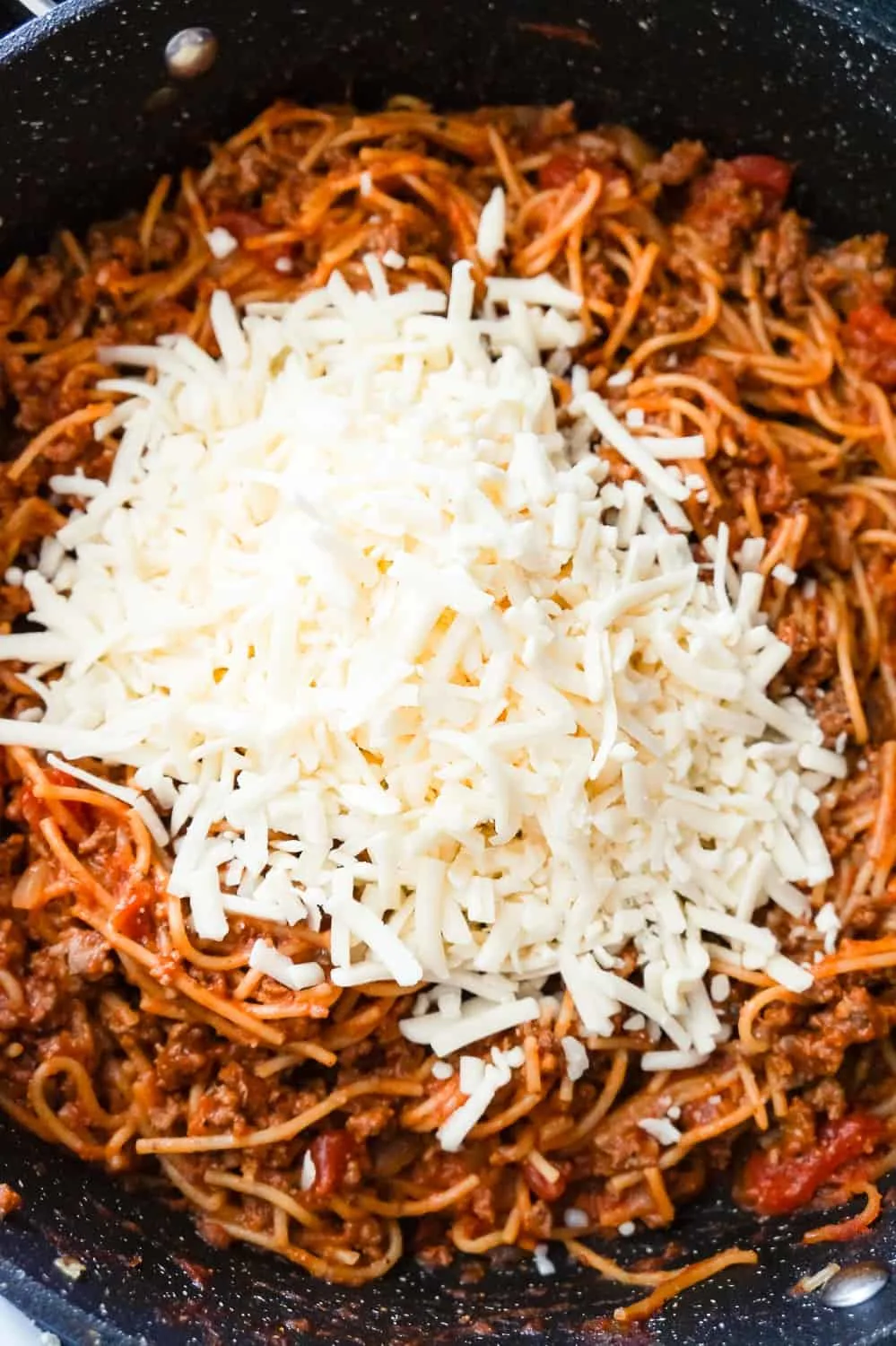 shredded mozzarella on top of spaghetti bolognese in a pan